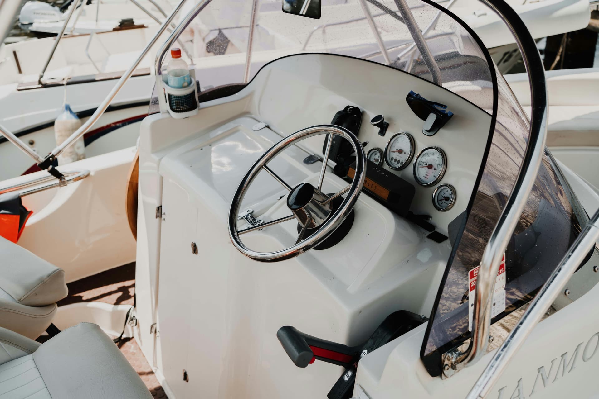 Boat dashboard with chrome steering wheel, analog meters and throttle, partial view of seats.